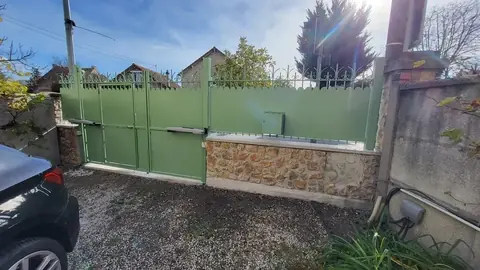 Portail battant et clôture brise-vue en acier vert sur muret en pierre